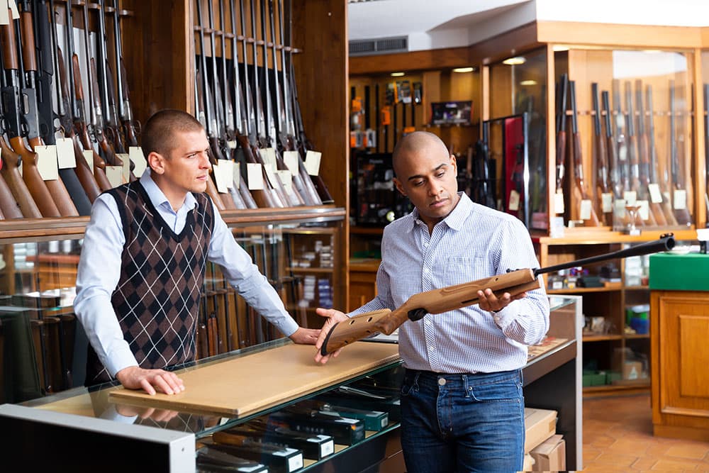 Man in gun store looking at hunting rifle